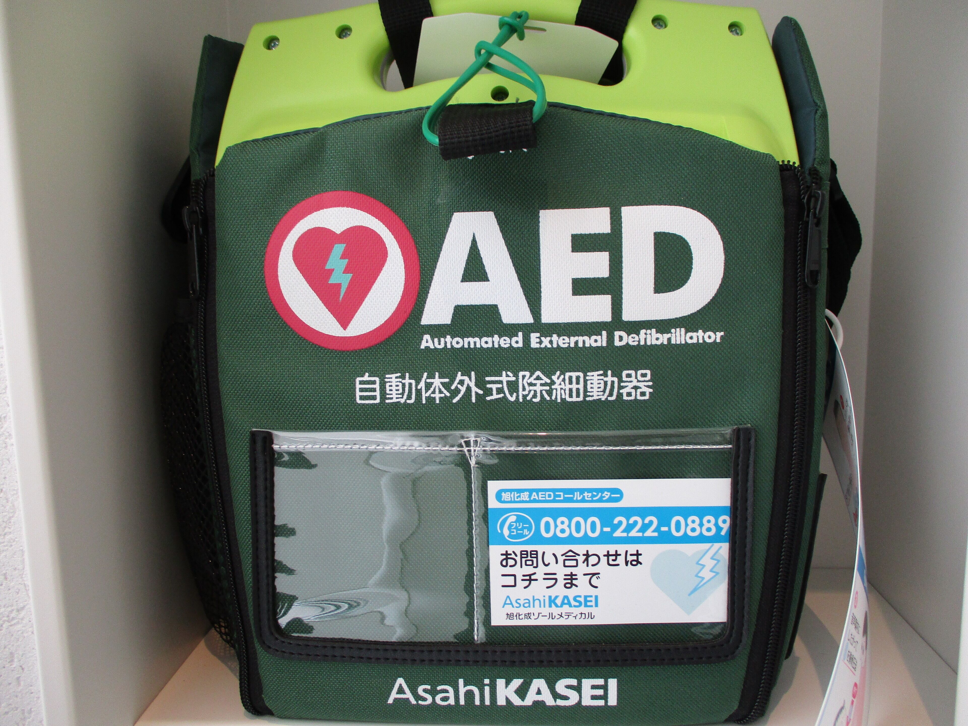 Bolsa verde y negra para desfibrilador externo automático (DEA) con un símbolo de corazón y el texto "Asahi KASEI".
