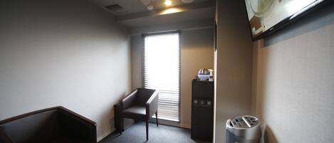 A small, dimly lit room with a single chair, a trash bin, and a window with blinds.