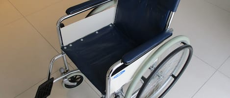 Una silla de ruedas con reposapiés y respaldo, sobre un piso de baldosas.