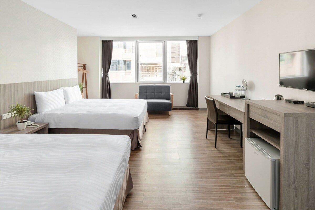 A hotel room with two beds, a desk, a chair, a television, and a window with curtains.