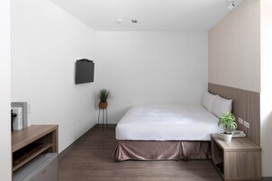 Habitación de hotel moderna con una cama grande, una mesita de noche con una planta, un escritorio pequeño con una computadora y un televisor montado en la pared.