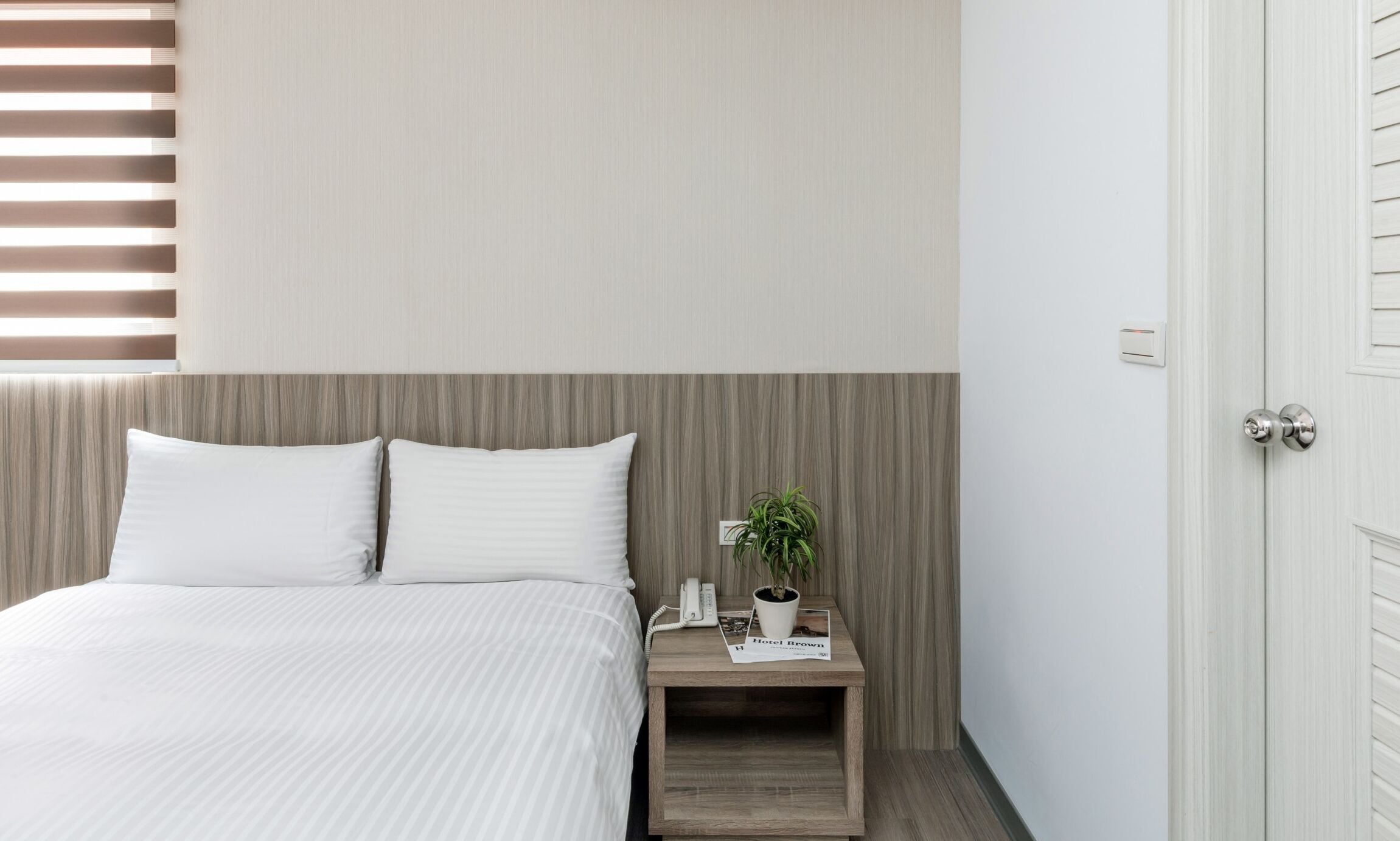 Quarto moderno com cama, duas almofadas, mesa de cabeceira com celular, planta e uma revista.