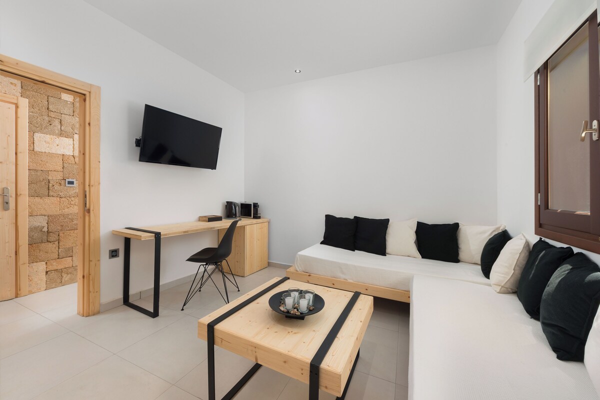 A modern living room with a sofa, a coffee table, a desk, and a TV mounted on the wall.