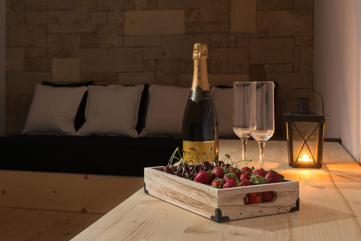 A wooden table with a bottle of champagne, two glasses, and a wooden crate of strawberries.