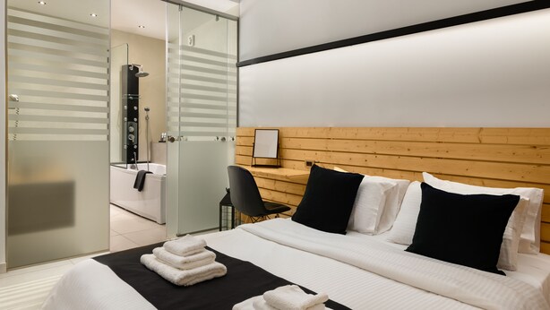 Una habitación de hotel moderna con una cama grande, cabecera de madera, un escritorio con silla y cabina de ducha de vidrio.