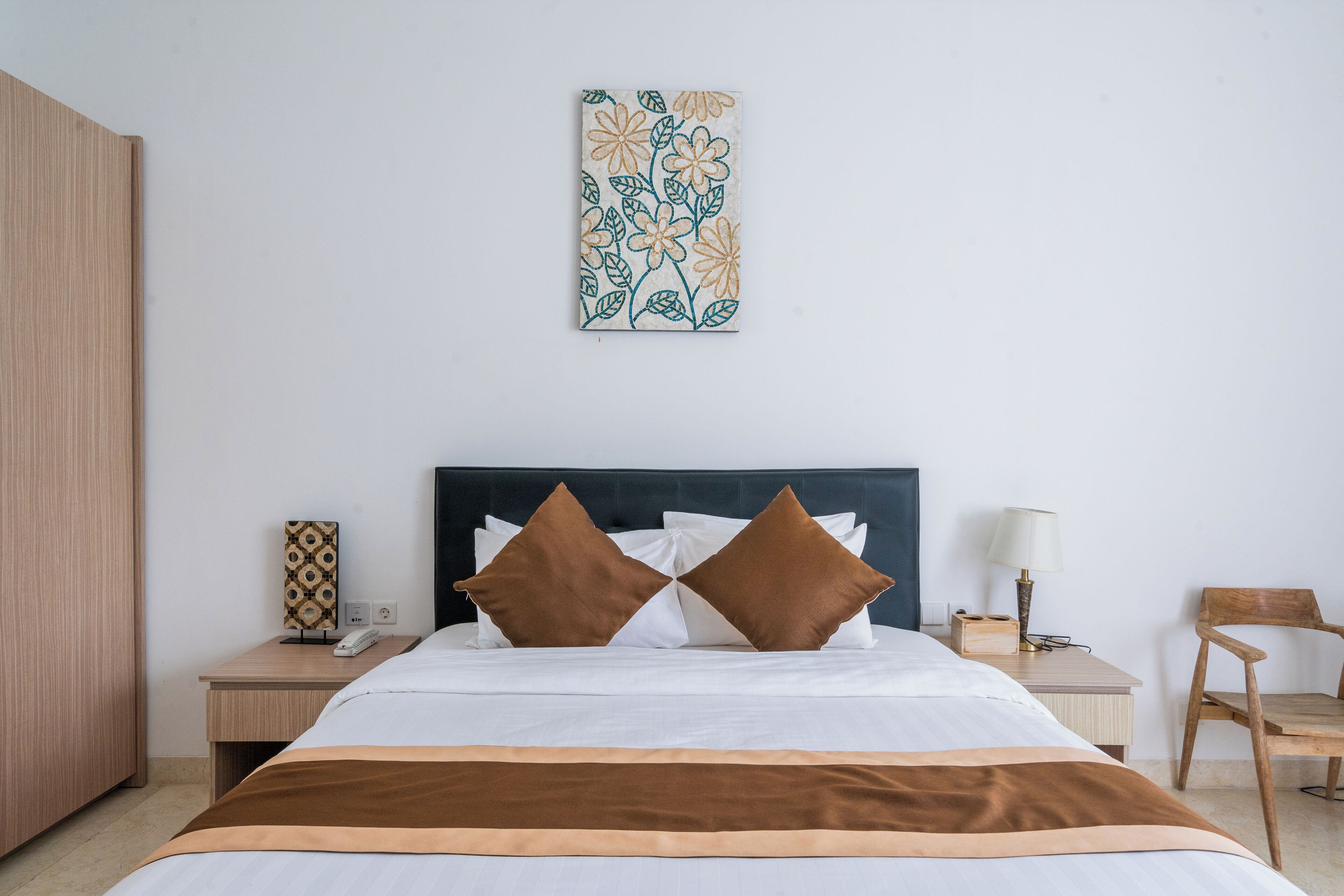 A hotel room with a bed, two nightstands, a chair, a lamp, and a wall-mounted artwork.