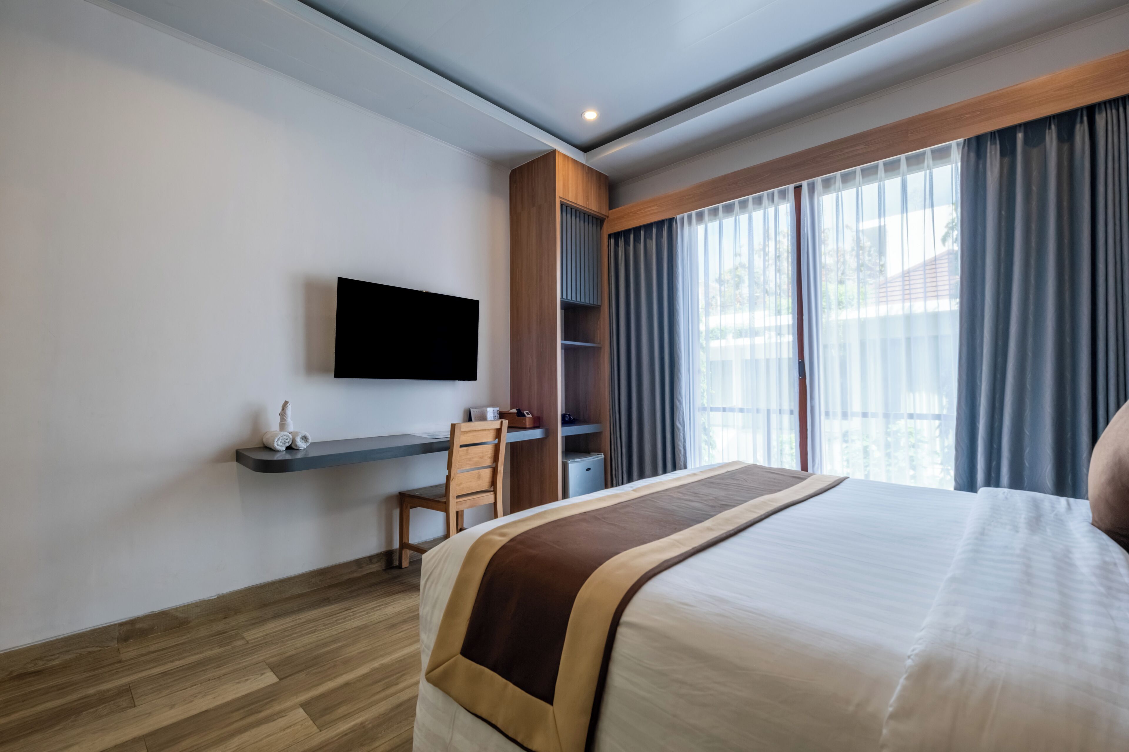 Hotelkamer met een bed, een bureau, een stoel, een televisie en een groot raam met gordijnen.