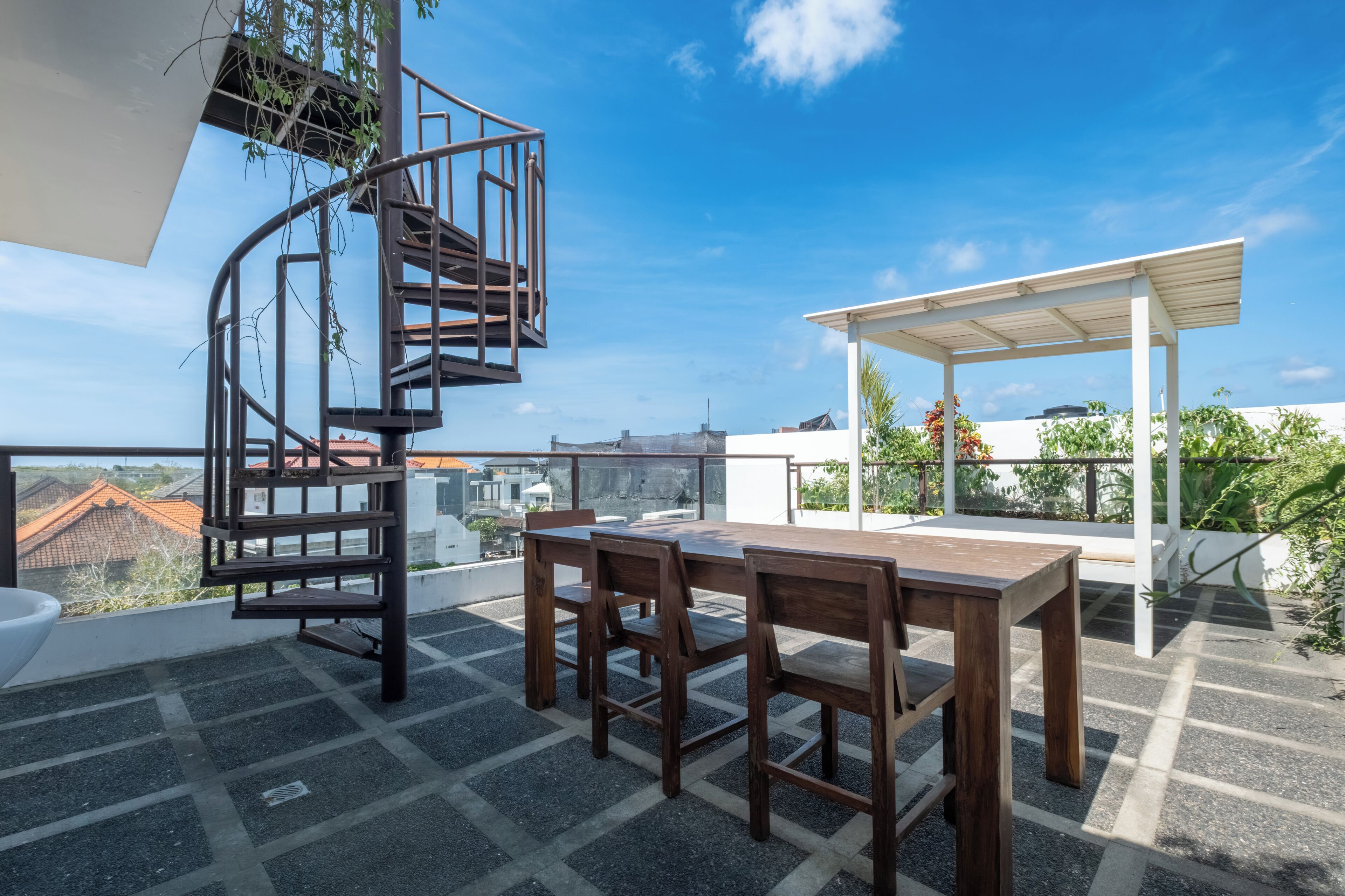 A rooftop terrace with a spiral staircase, a wooden table with chairs, and a covered seating area.