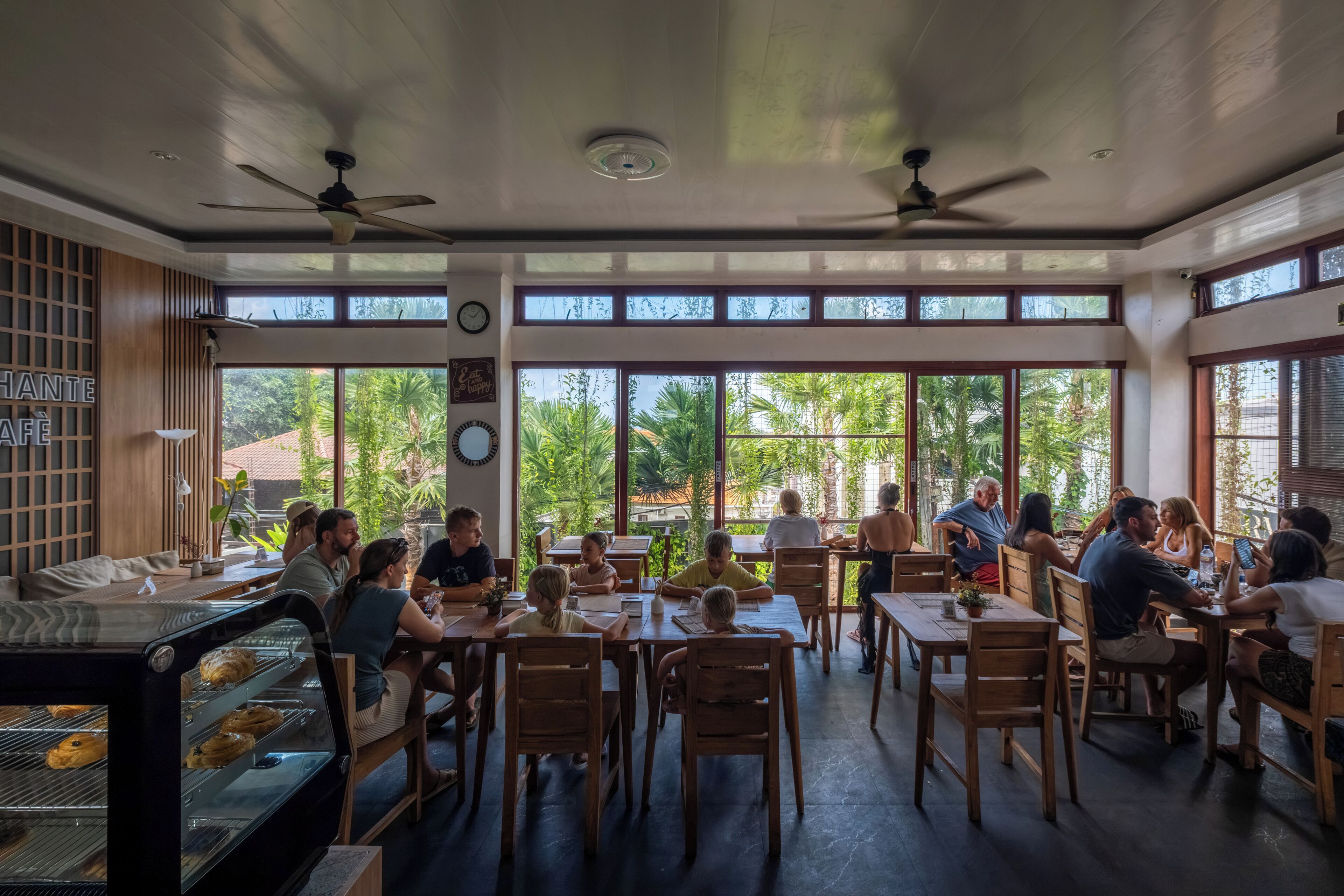 A restaurant with wooden furniture, large windows, and ceiling fans.