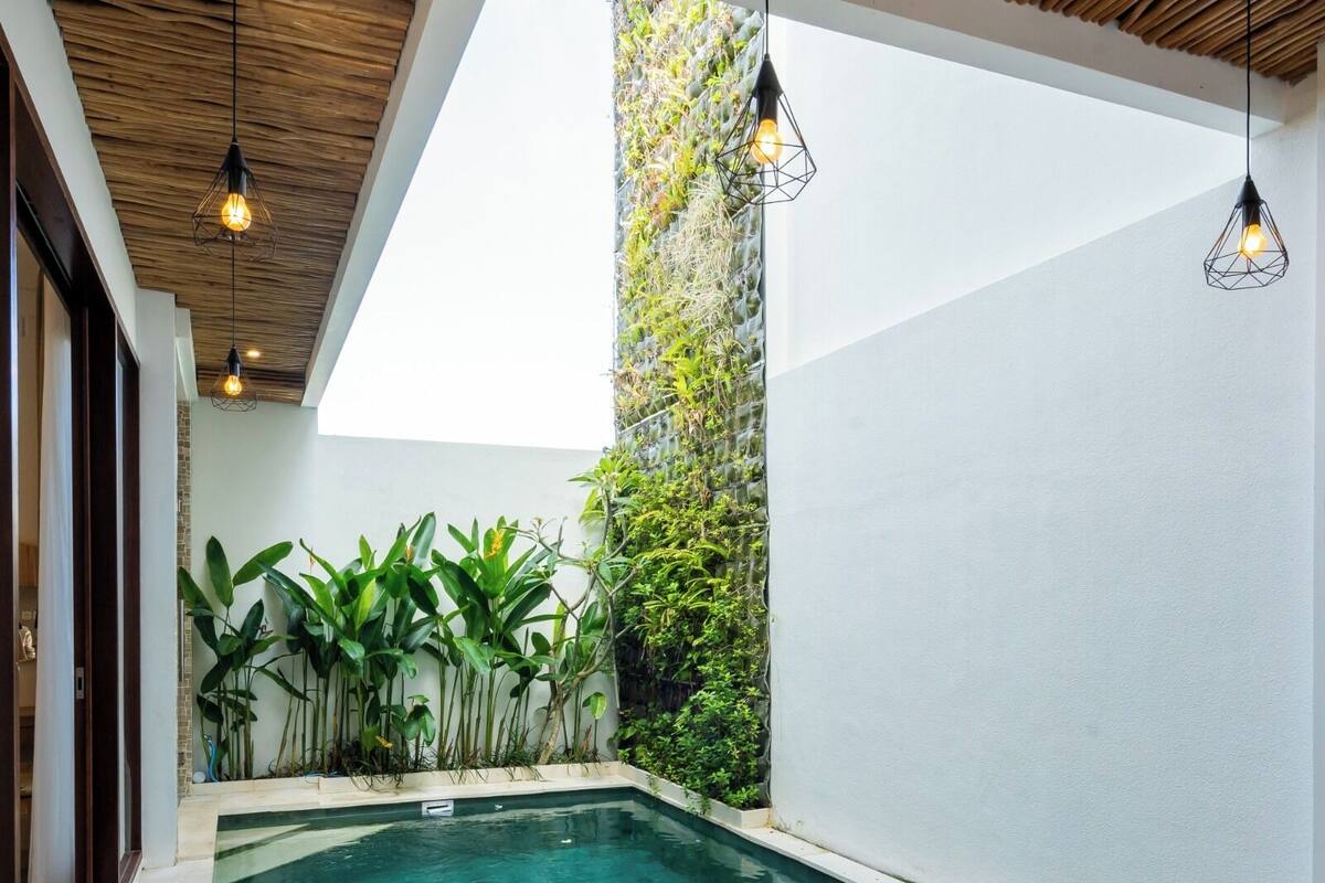 A modern indoor pool area with a clear view of the sky, surrounded by lush greenery and a wooden ceiling.