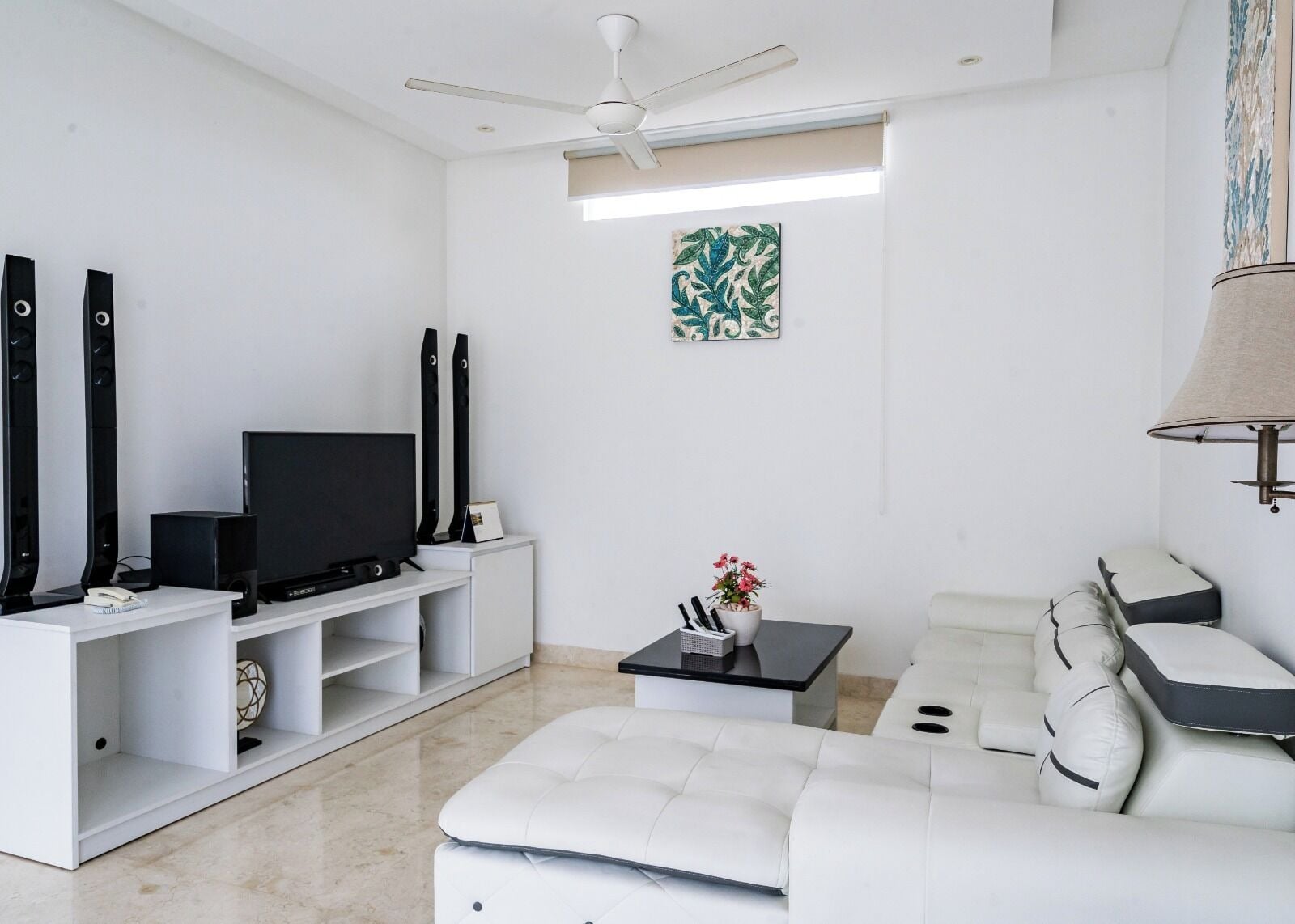 A modern living room with a flat-screen TV, white sofas, a coffee table, and a ceiling fan.