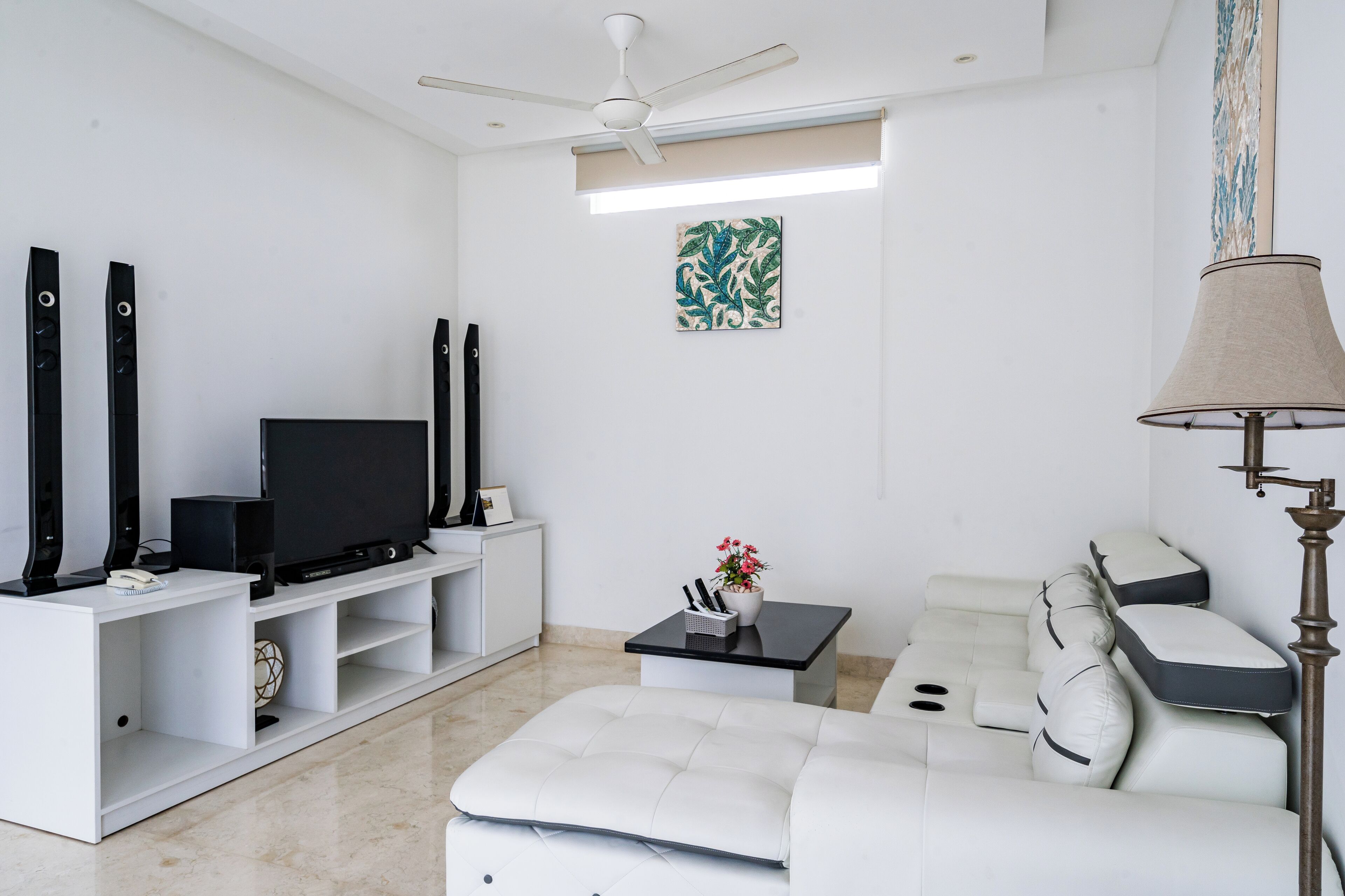 A modern living room with a flat-screen TV, white sofas, a coffee table, and a ceiling fan.