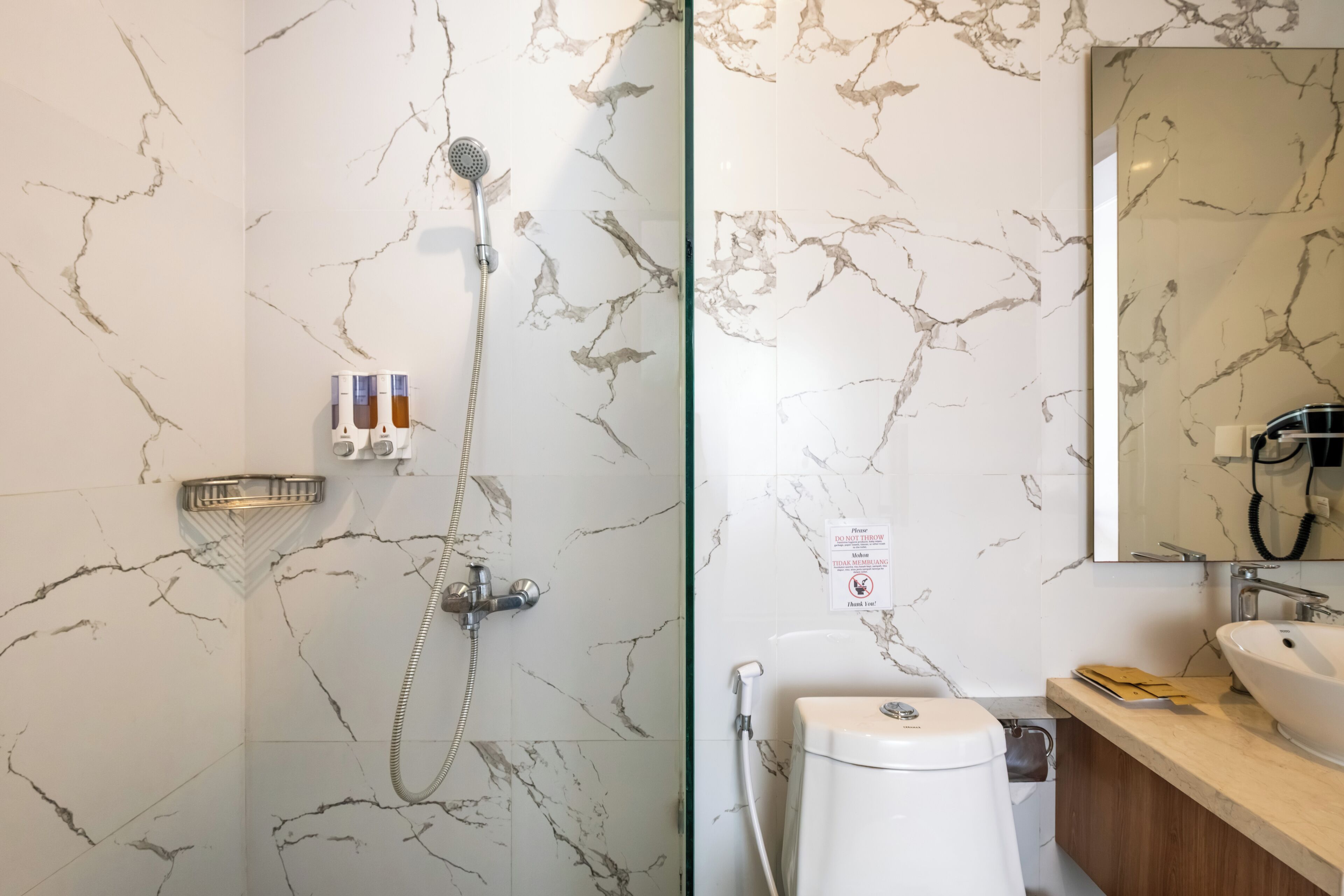Baño con ducha, inodoro, lavabo y paredes de mármol.