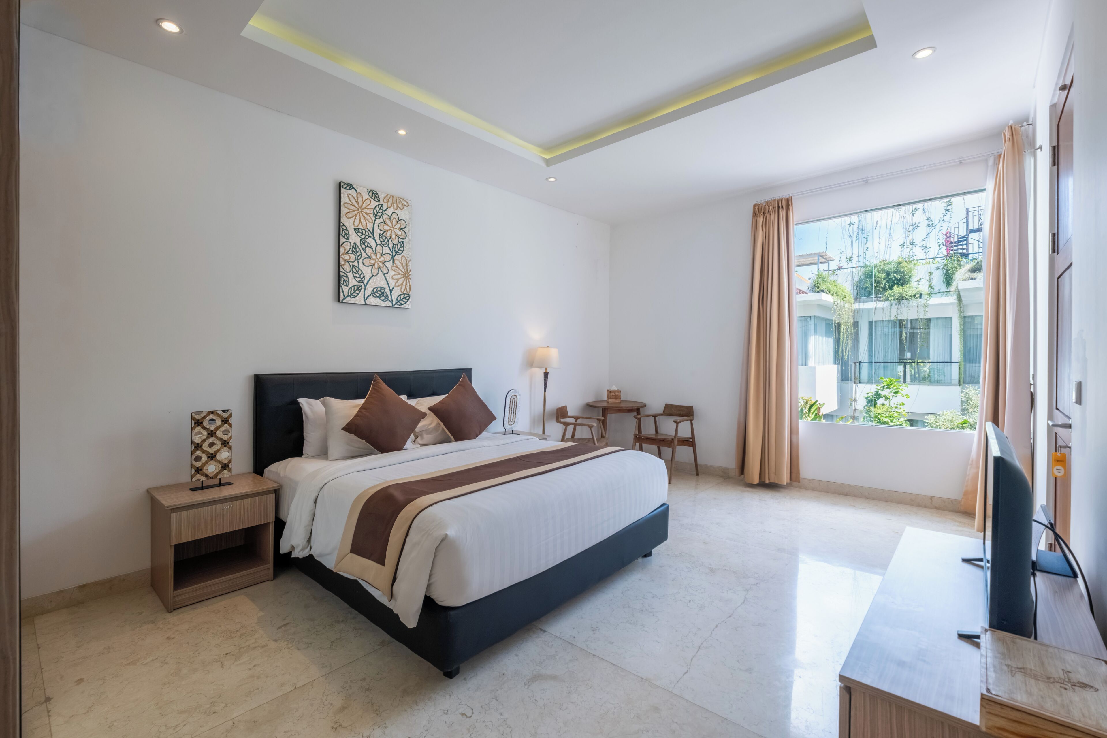A modern hotel room with a large bed, bedside tables, a desk, and a view of greenery outside.