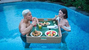 Two people dining by a poolside with a wicker table holding plates of food and drinks. - Bali Residence Villa (Ungasan)