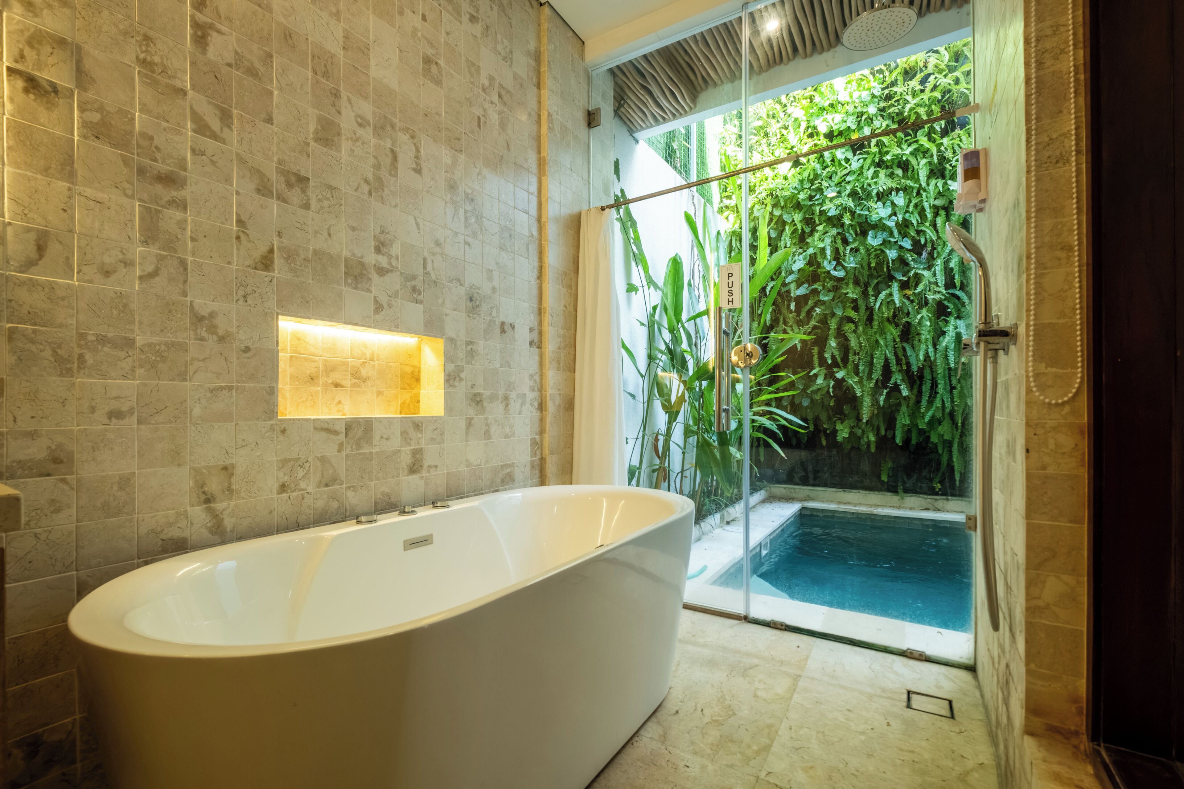 A modern bathroom with a freestanding bathtub, a glass shower enclosure, and a view of a lush garden.