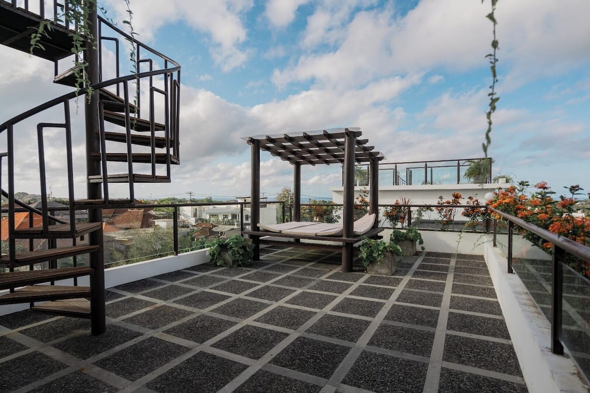 A rooftop terrace with a pergola, a swing, and potted plants.