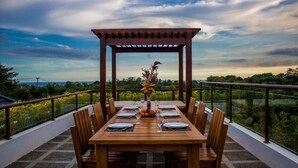 A wooden dining table set for six with a pergola overhead, surrounded by chairs, overlooking a scenic landscape. - Bali Residence Villa (Ungasan)