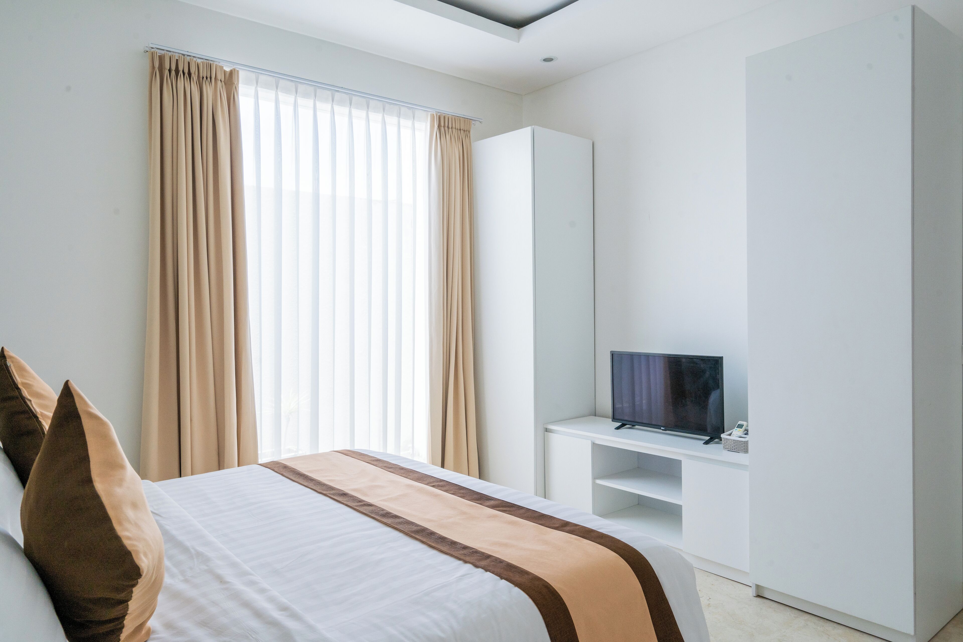 A hotel room with a bed, a TV on a white stand, and a wardrobe.