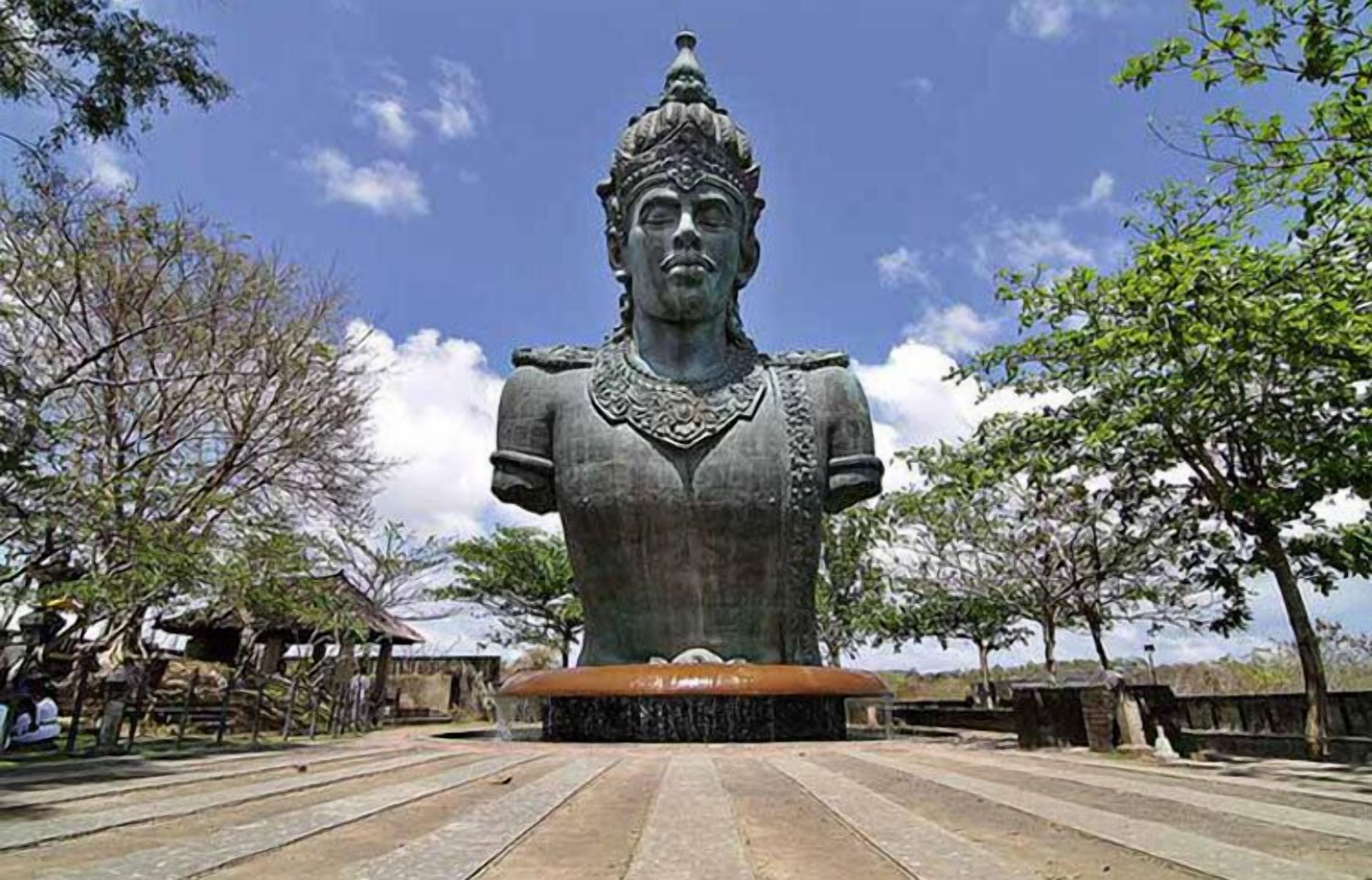 A large bronze statue of a figure with elaborate attire, set on a stone platform with a clear sky in the background.