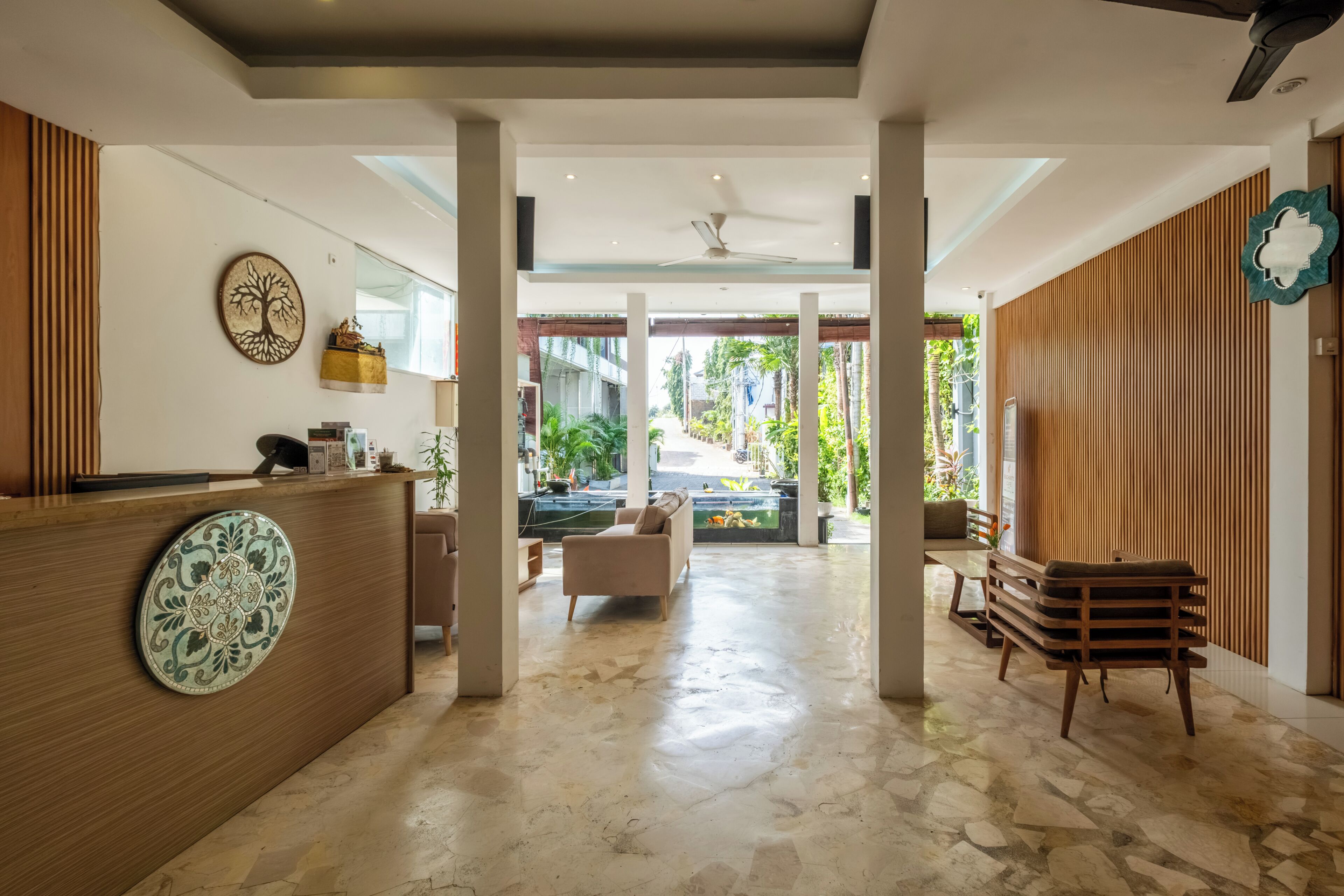 A hotel lobby with a reception desk, seating area, and a view of the outdoor garden.
