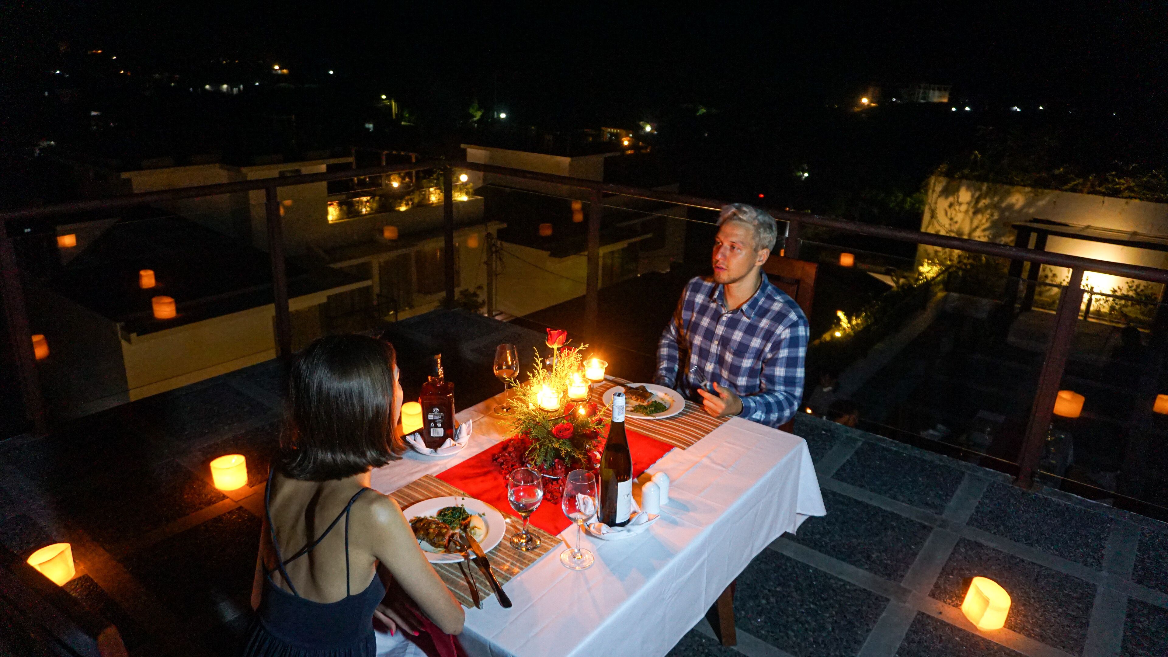 A couple dining at an outdoor table with candles, wine, and a bottle of champagne.