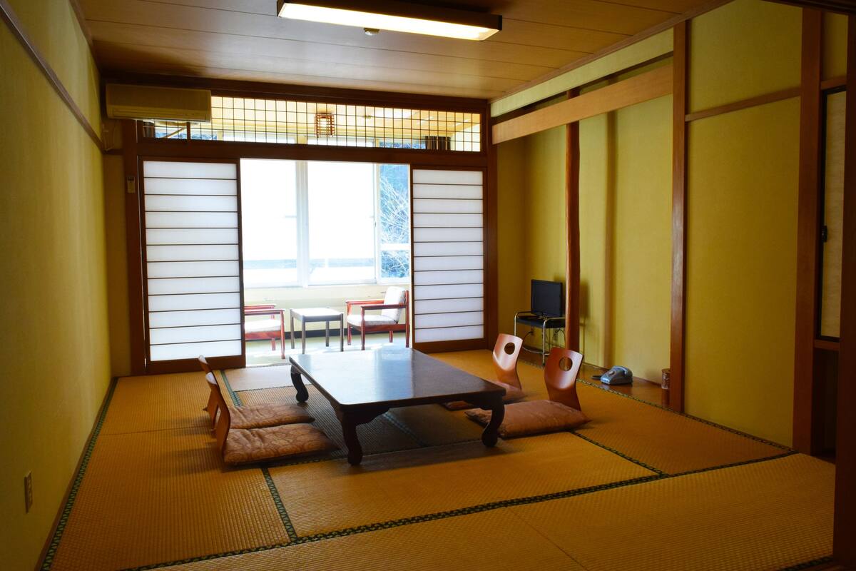 Ein traditioneller japanischer Raum mit Tatami-Böden, einem niedrigen Tisch und verschiebbaren Türen.