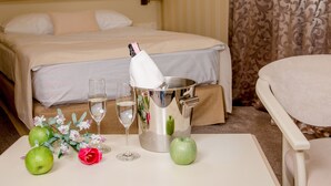 Una camera d'albergo con un letto, un tavolo con delle mele, un bicchiere d'acqua, una bottiglia di champagne e un bouquet di fiori.