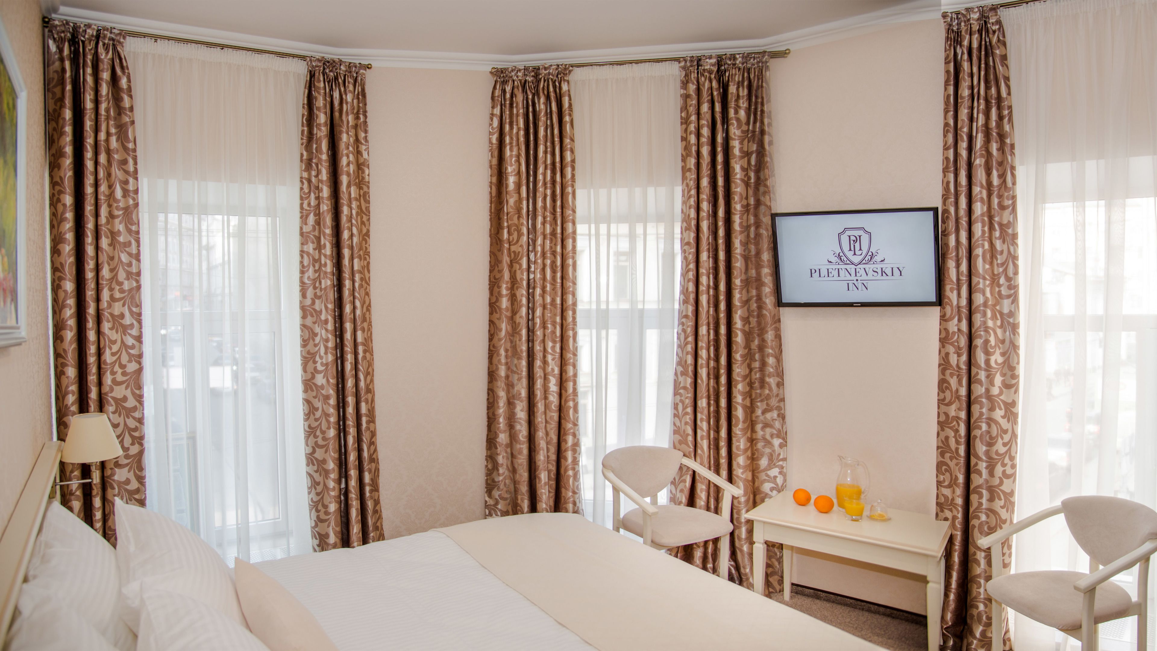 Een hotelkamer met een bed, een bureau met twee stoelen, een televisie aan de muur en een raam met gordijnen.