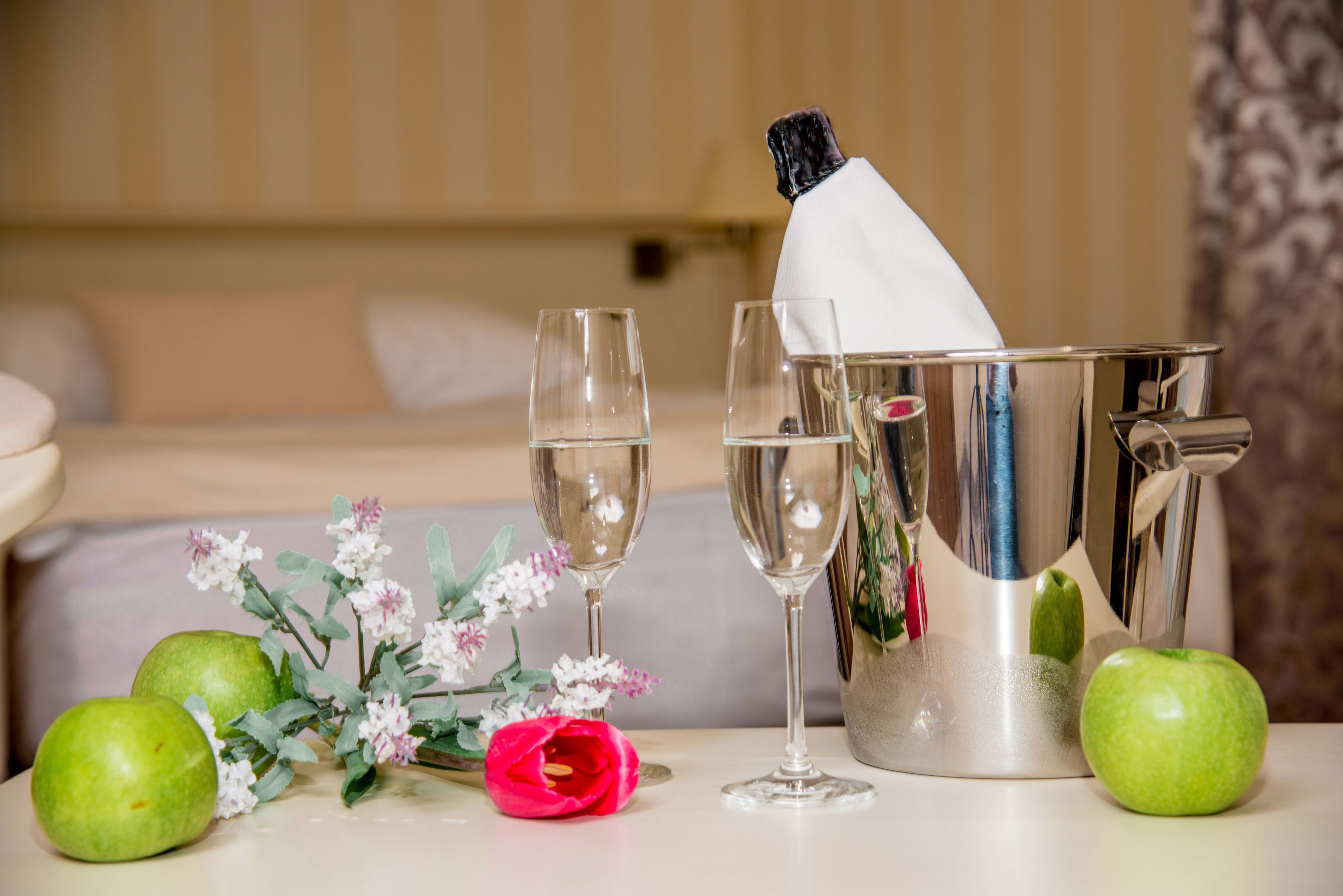 A table with a champagne bucket, two glasses, and green apples.