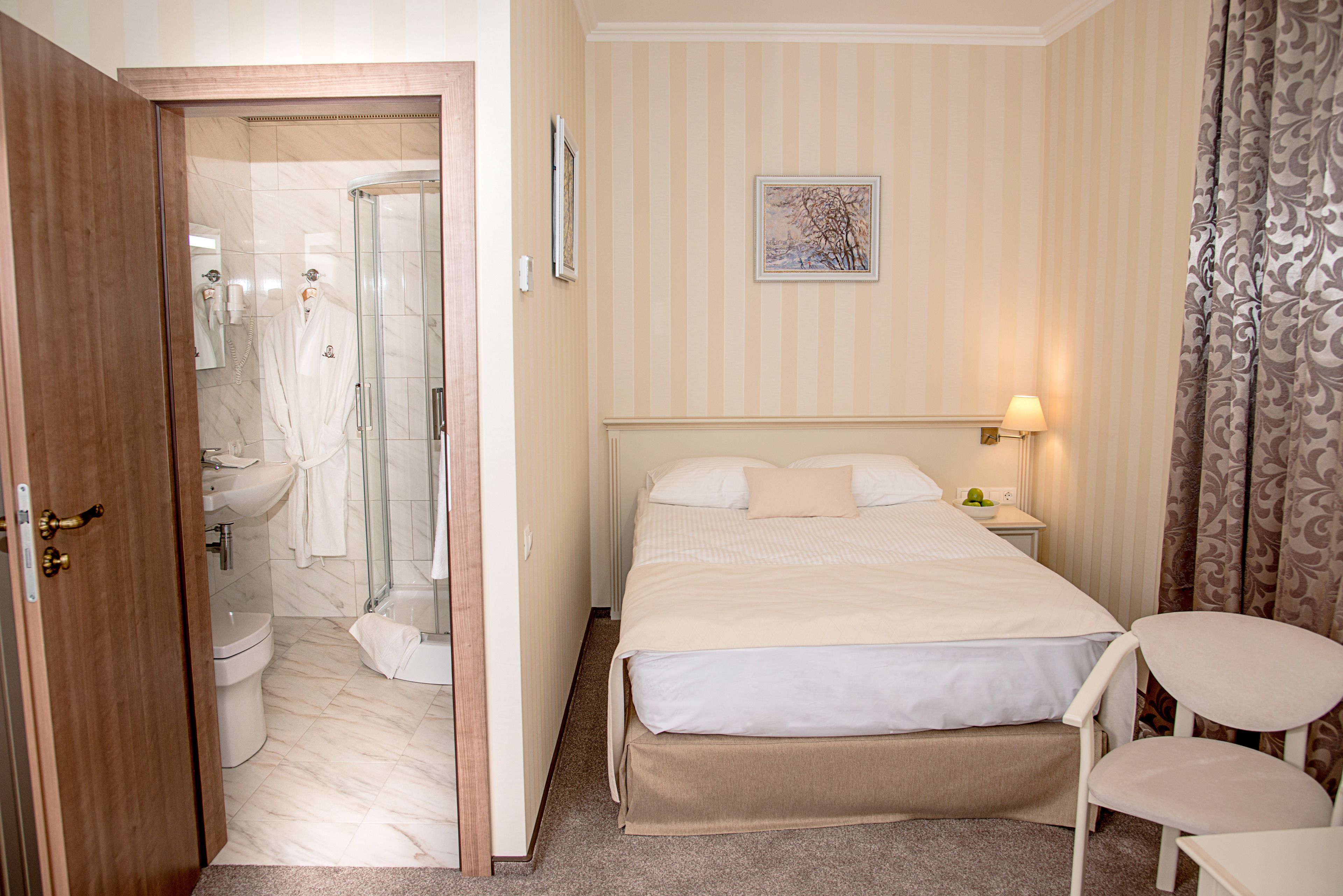 A hotel room with a bed, a chair, a bedside table with a lamp, a shower area, and a toilet.