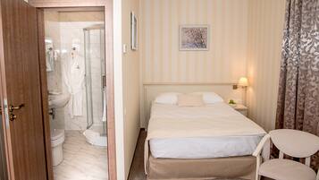 A hotel room with a bed, a chair, a bedside table with a lamp, a shower area, and a toilet.