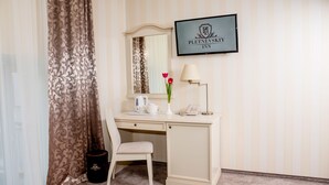 Una camera d'albergo con una scrivania, una sedia, uno specchio, una targa incorniciata e un vaso con fiori.
