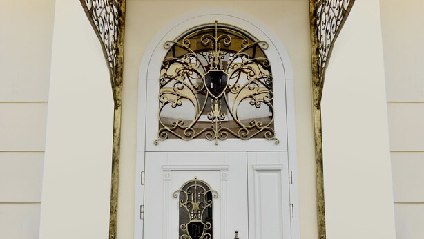 Una porta bianca con decorazioni in ferro battuto e uno stemma araldico.