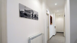Een gang met een radiator, een lijst met een foto aan de muur, en een deur aan het einde.