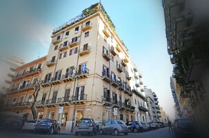 Un edificio a più piani con balconi, un segnale di parcheggio e auto parcheggiate.