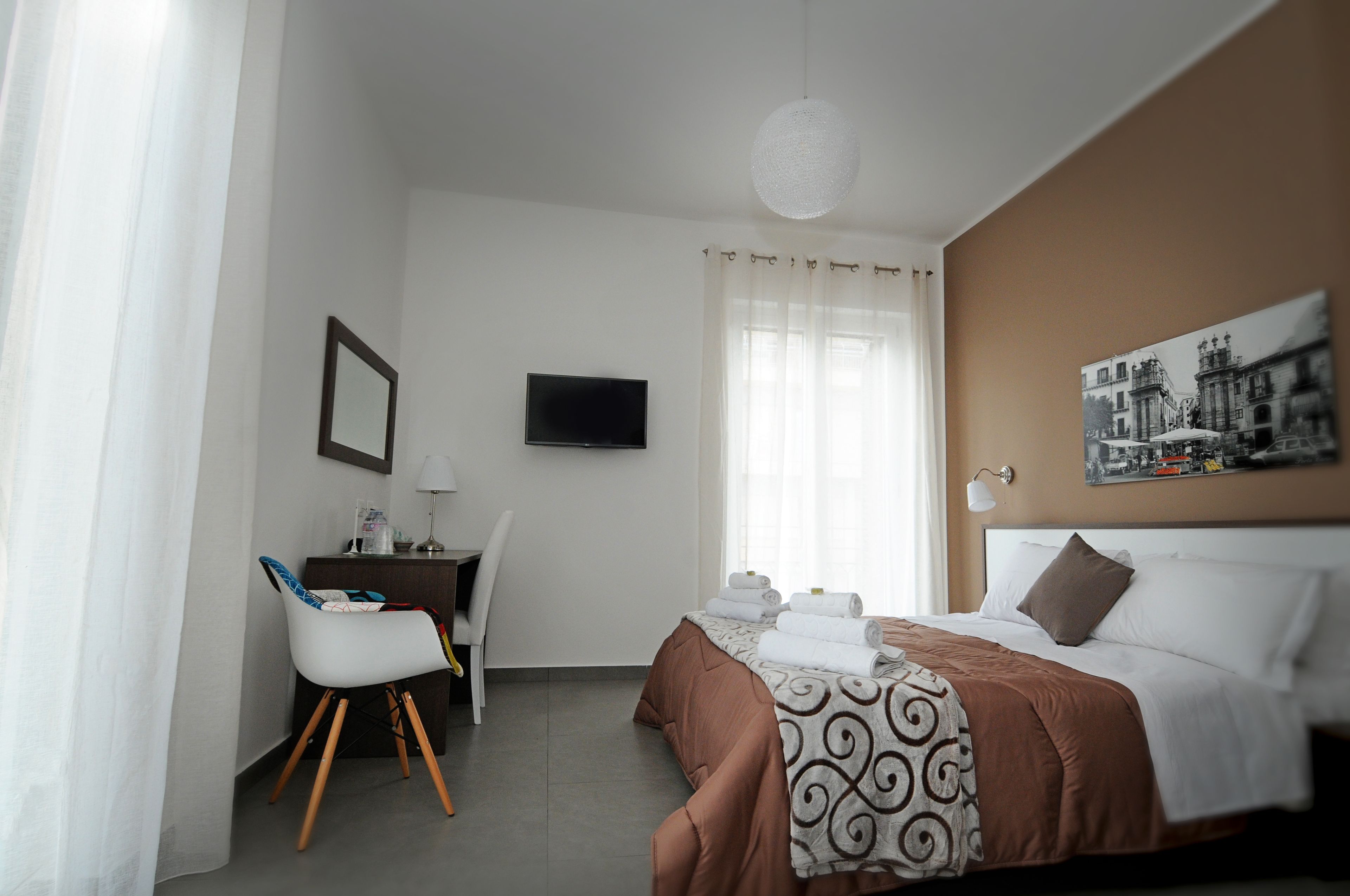 A hotel room with a bed, a desk, a chair, a television, and a window with curtains.