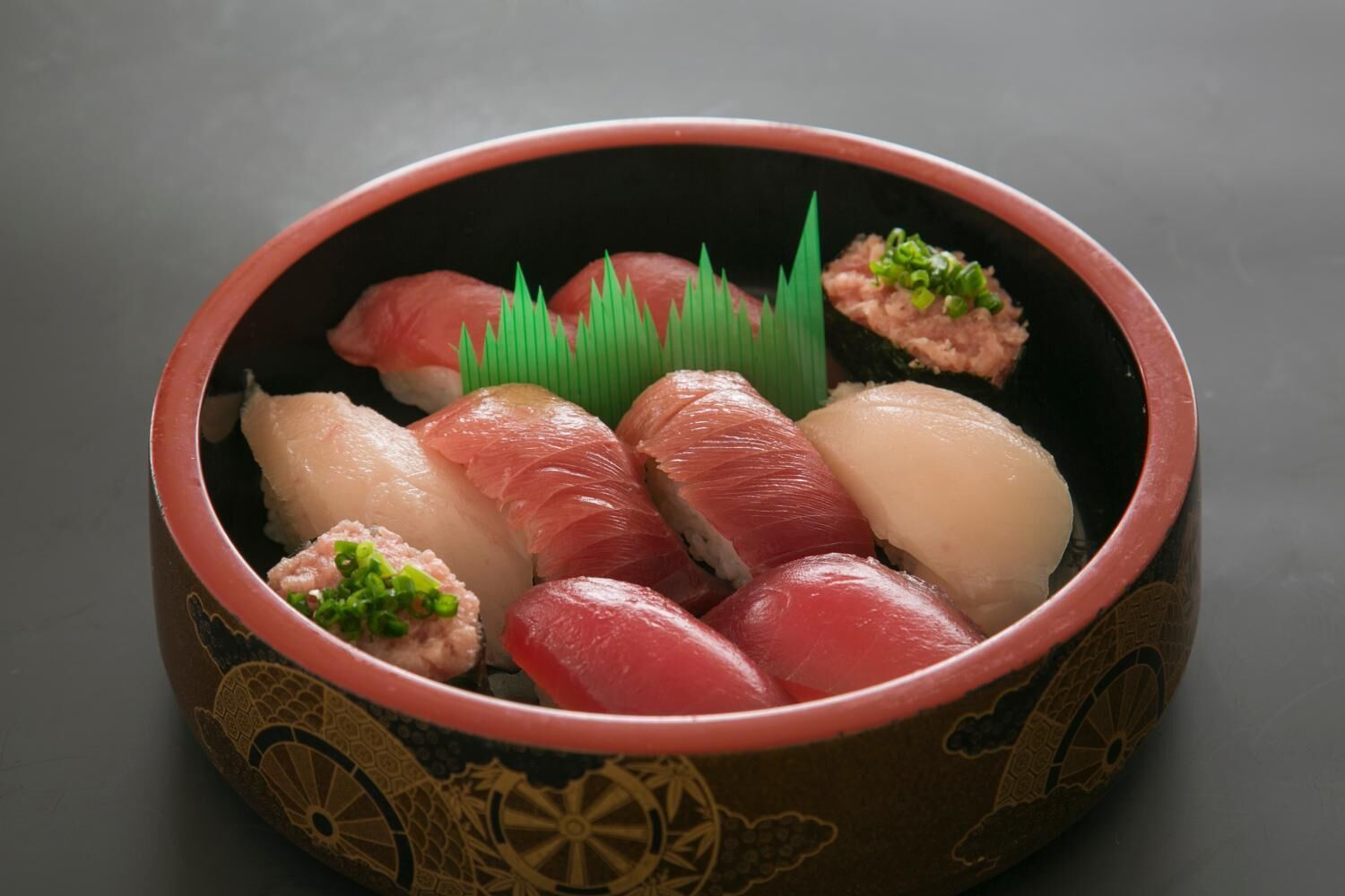 A bowl of sushi with various types of fish, garnished with green onions.