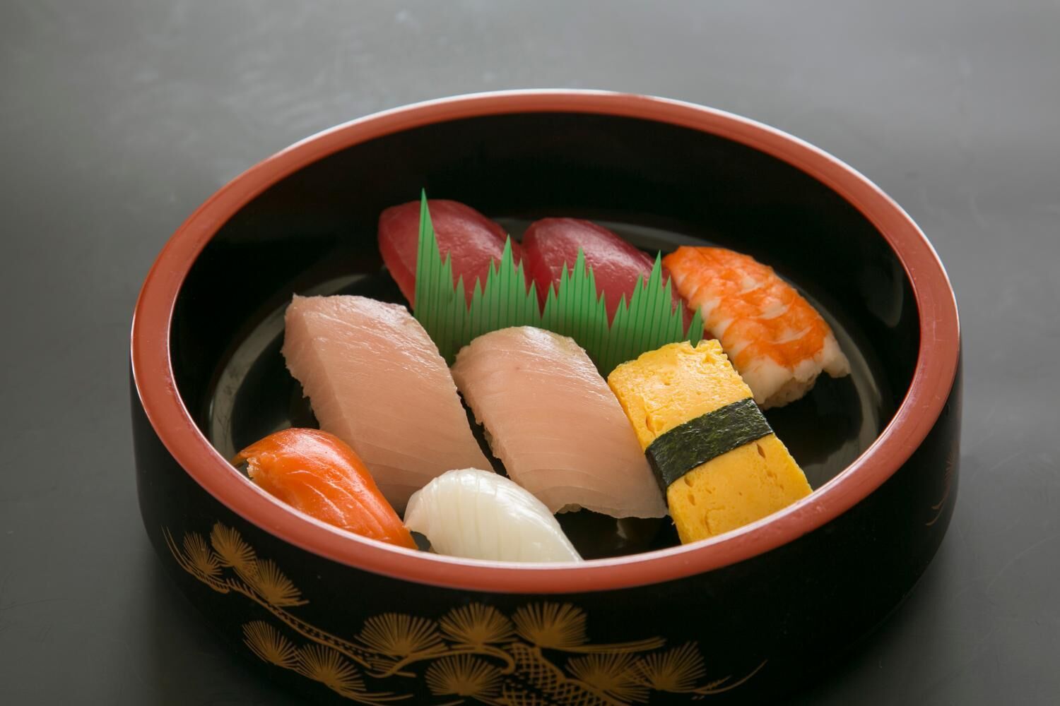 A bowl of sushi with various types of fish and a decorative leaf.