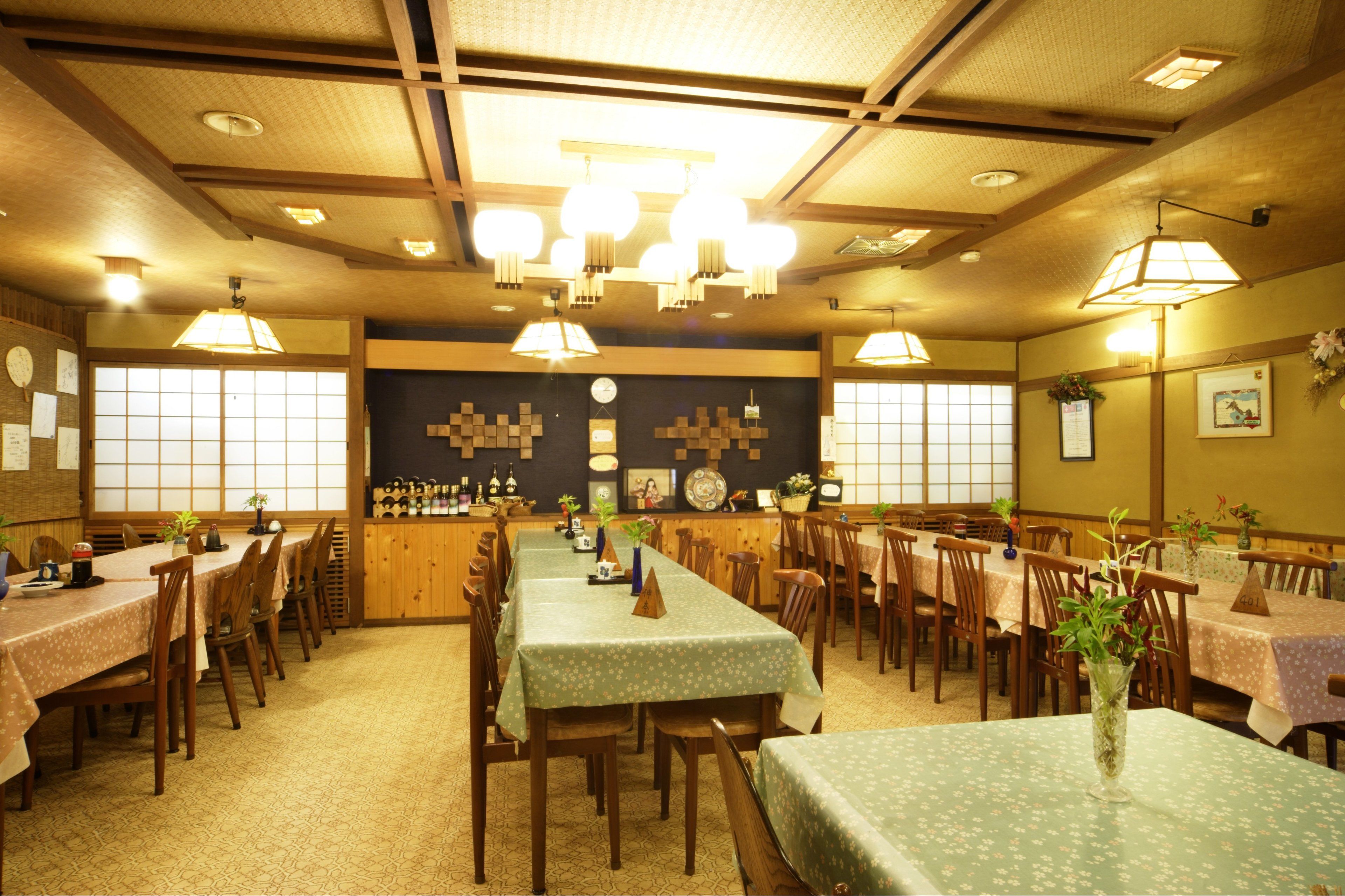 A traditional Japanese restaurant with multiple wooden tables and chairs, a central counter, and a decorative wall with a clock and framed pictures.
