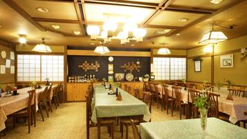 A traditional Japanese restaurant with multiple wooden tables and chairs, a central counter, and a decorative wall with a clock and framed pictures.