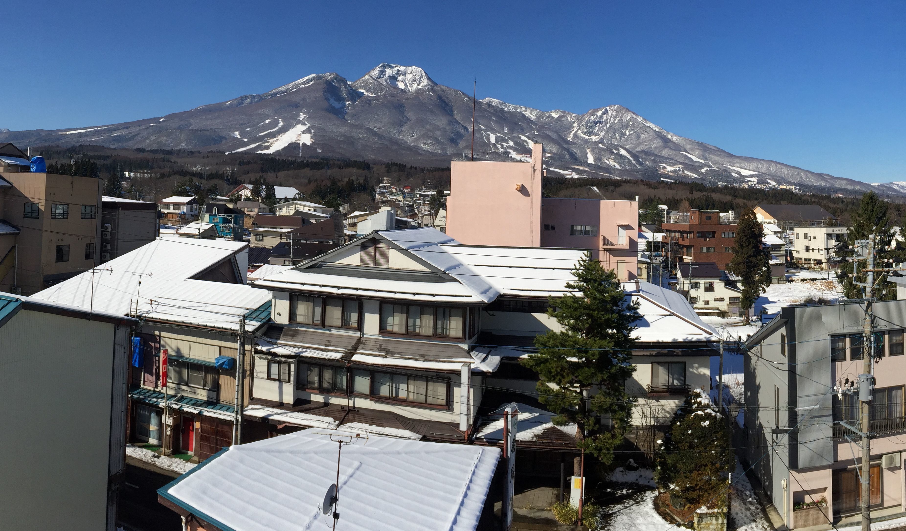 A residential area with traditional architecture, a prominent snow-capped mountain in the background, and a clear sky.