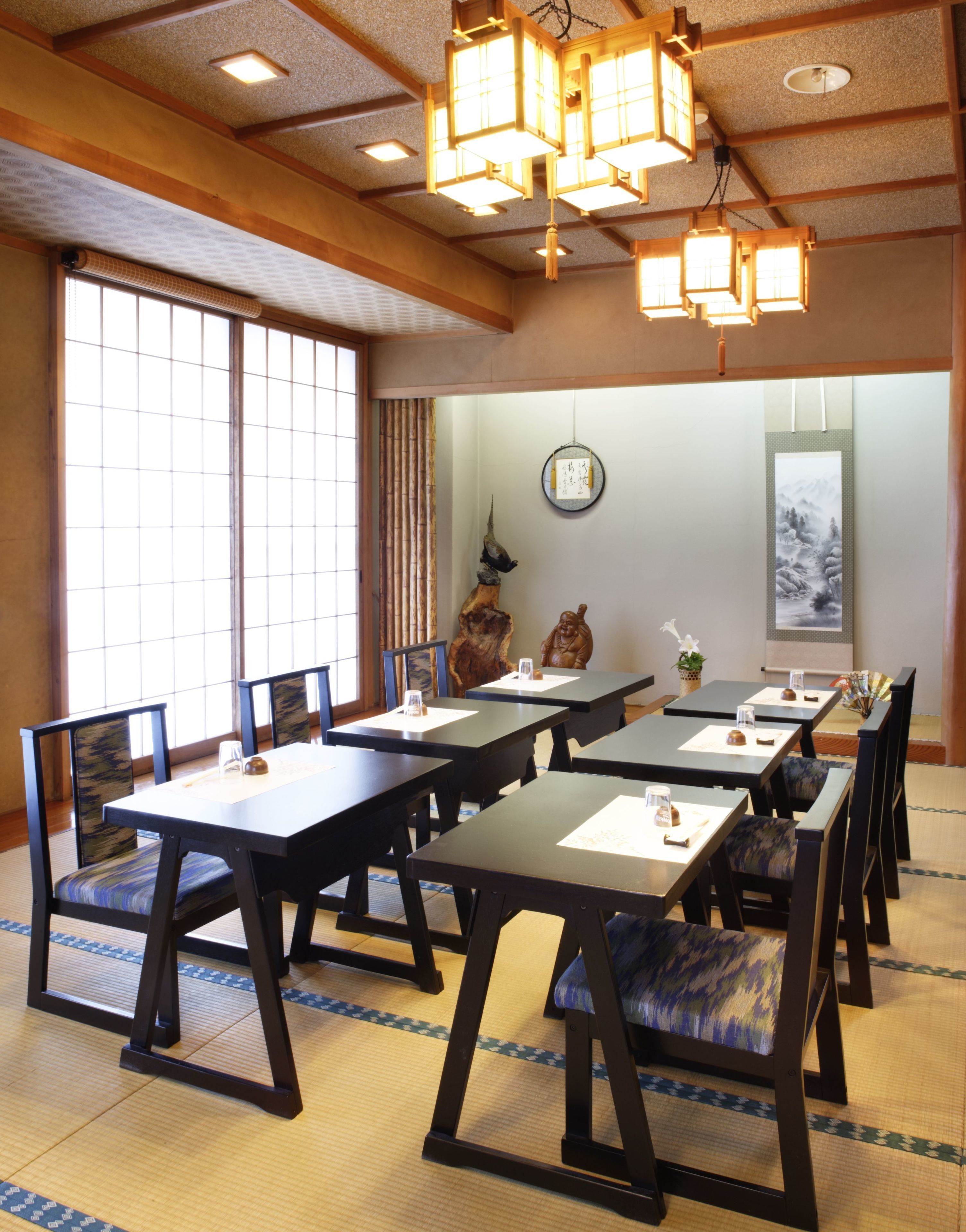 A traditional Japanese-style dining room with tatami mat flooring, low tables, and dark wooden chairs.