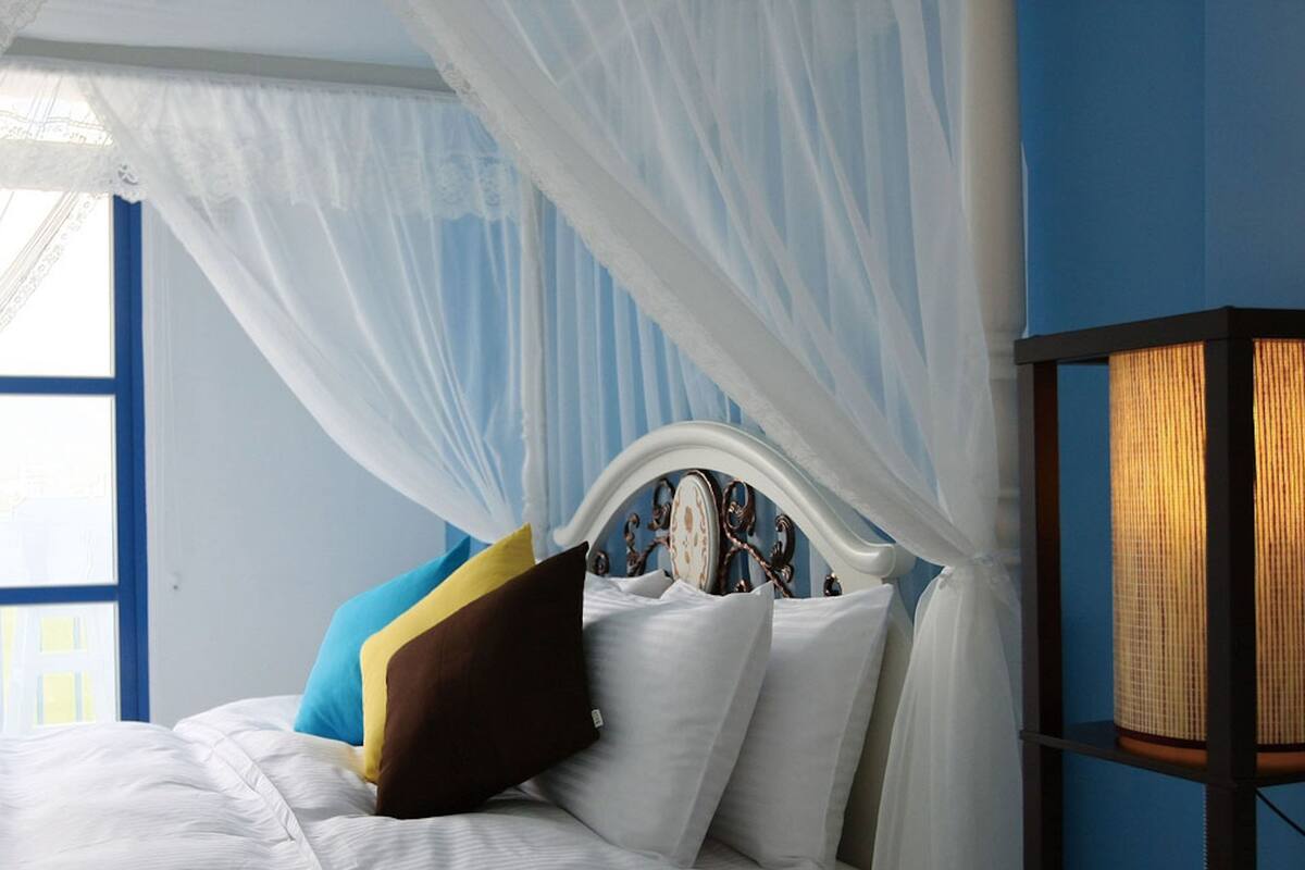 Ein Bett mit weißer Bettwäsche, blau und braunen Kissen und einem Baldachin.