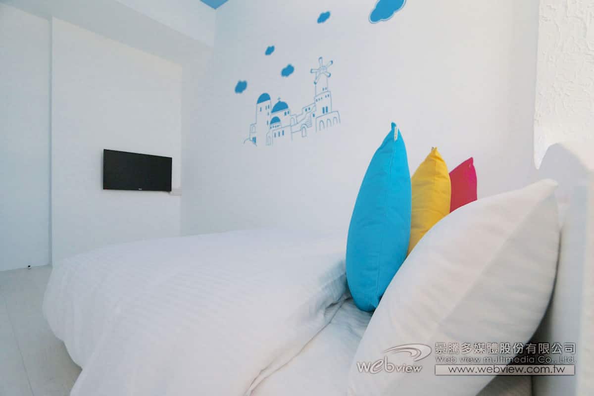 Ein Schlafzimmer mit einem Bett, einem flachbildfernseher an der Wand und farbenfrohen Kissen.