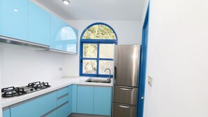 Une cuisine moderne avec des armoires bleues, un réfrigérateur en acier inoxydable et une fenêtre dotée d’un cadre bleu.