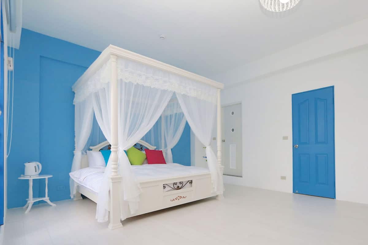 Ein Schlafzimmer mit Himmelbett, einem kleinen Tisch mit Wasserkocher und einer blauen Tür.