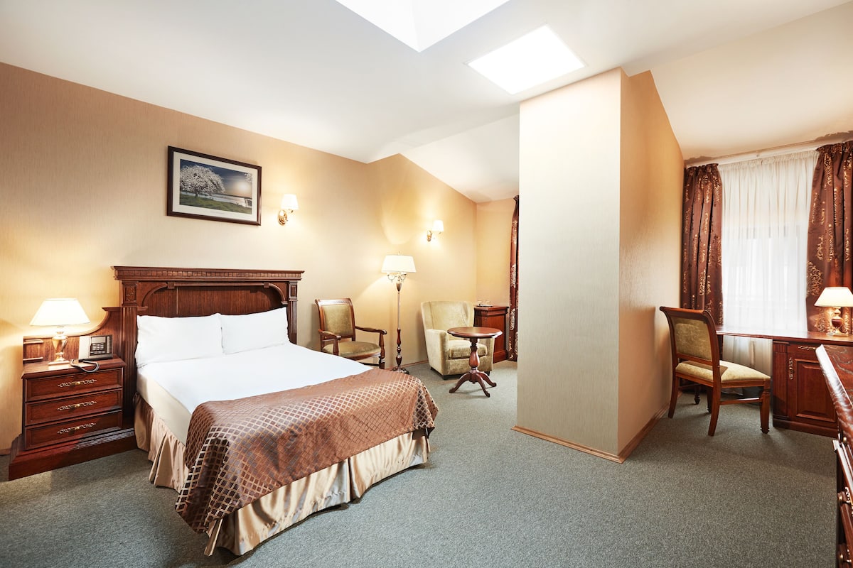 Hotellihuone, jossa on suuri sänky, kaksi tuolia, työpöytä ja pieni pöytä.