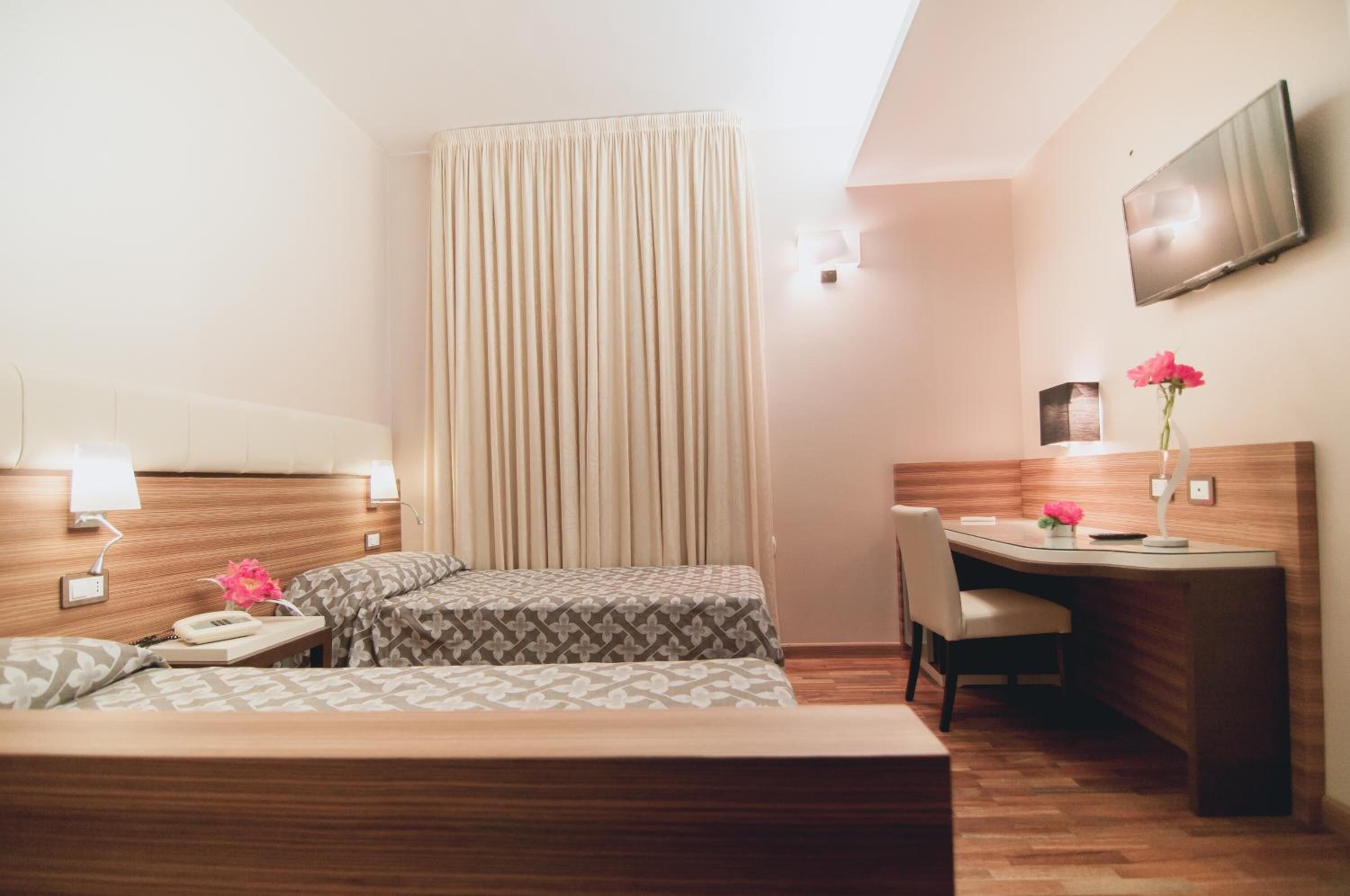Quarto de hotel com duas camas, uma escrivaninha, uma cadeira, uma televisão e uma cortina.