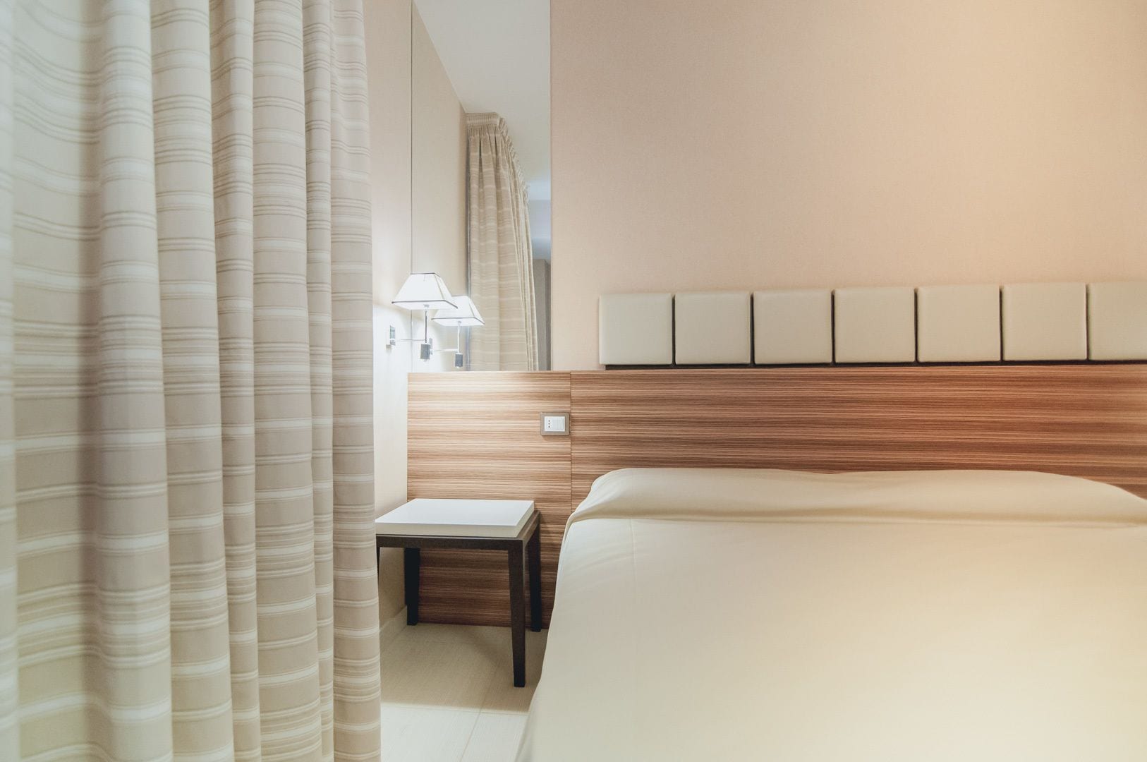 A modern hotel room with a large bed, a bedside table, a lamp, and a headboard with a light panel.